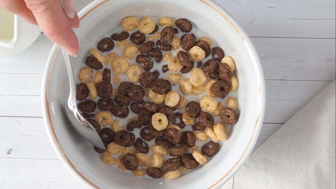 在一个白色的碗里晾干谷物早餐，倒入牛奶和混合，巧克力和玉米片，一顿健康的饭。视频素材