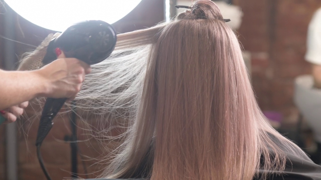 工作室的美发师用吹风机为女顾客吹头发视频素材