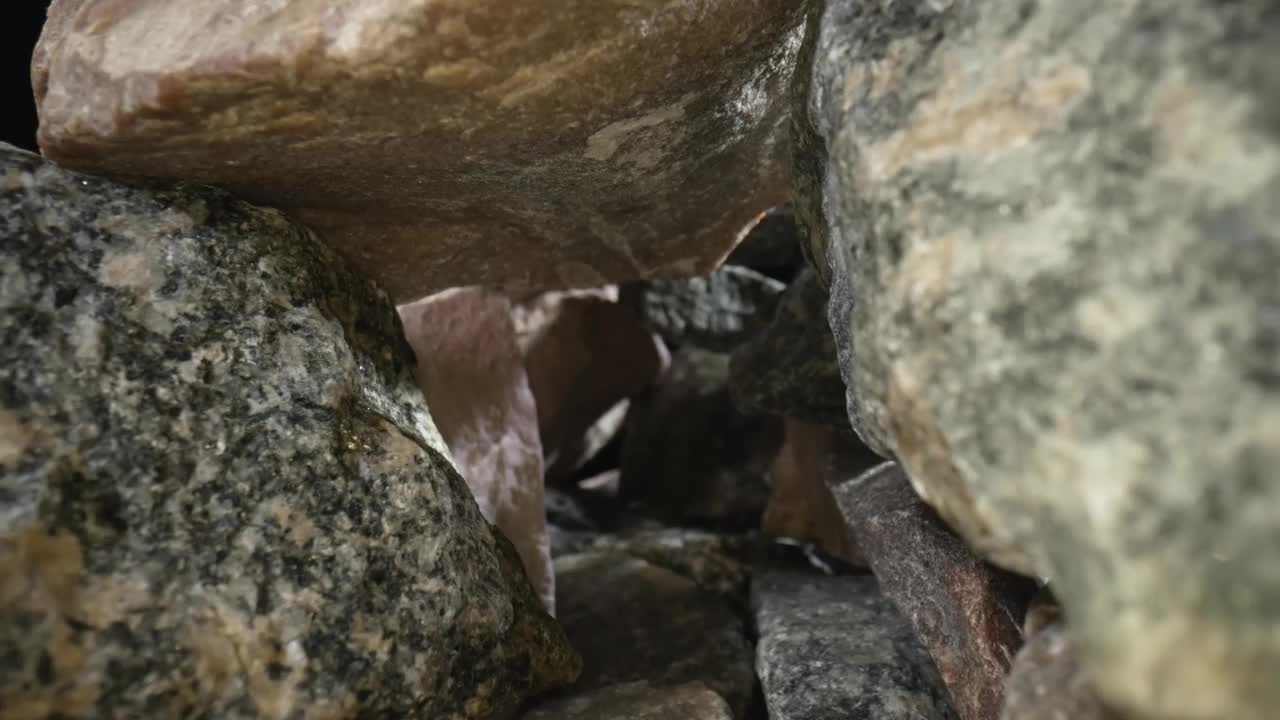 相机在黑色背景下的一堆灰色和棕色花岗岩中摇摄。粗糙的花岗岩砾石鹅卵石具有自然的纹理和断裂模式。地质学。石峡近景视频素材