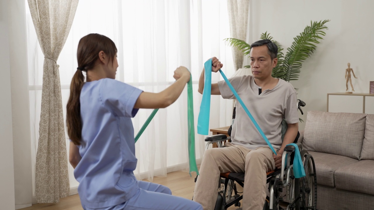 帮助退休男性轮椅使用者使用阻力带进行物理治疗的亚洲个人住院护理员。居家老年人健身理念视频下载