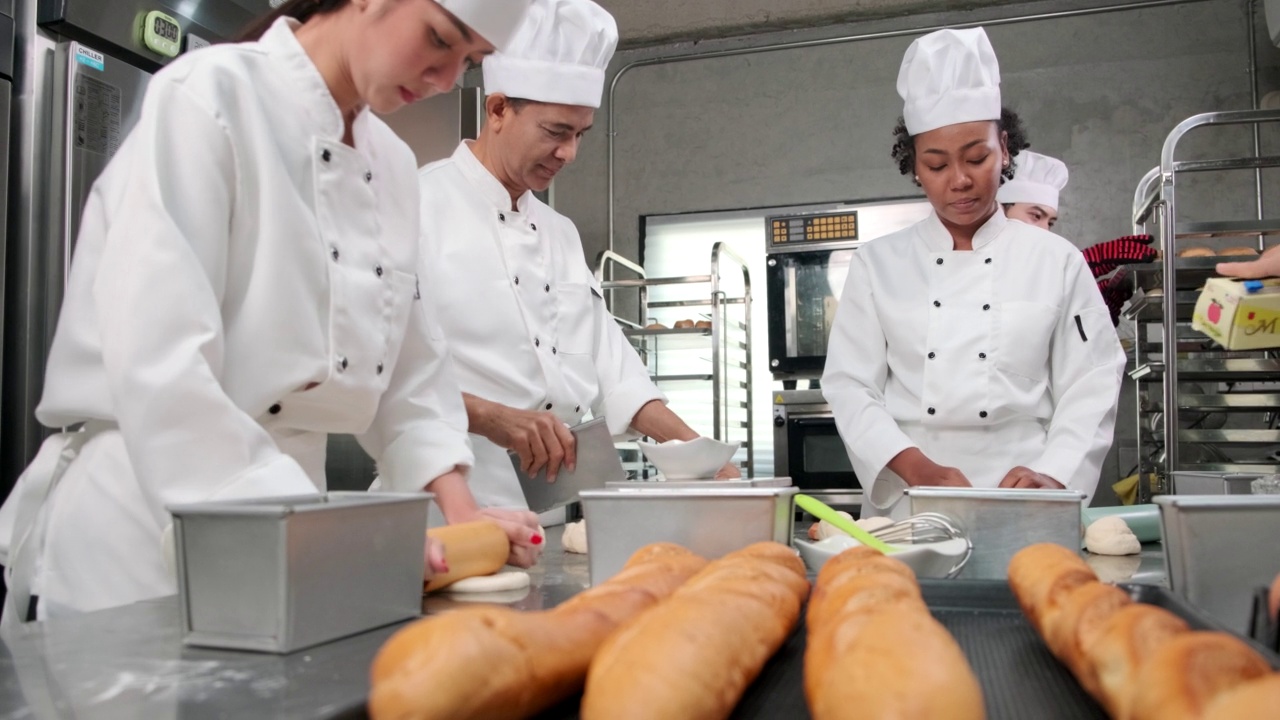 穿着制服的厨师团队准备在不锈钢厨房里烤面包和糕点。视频下载