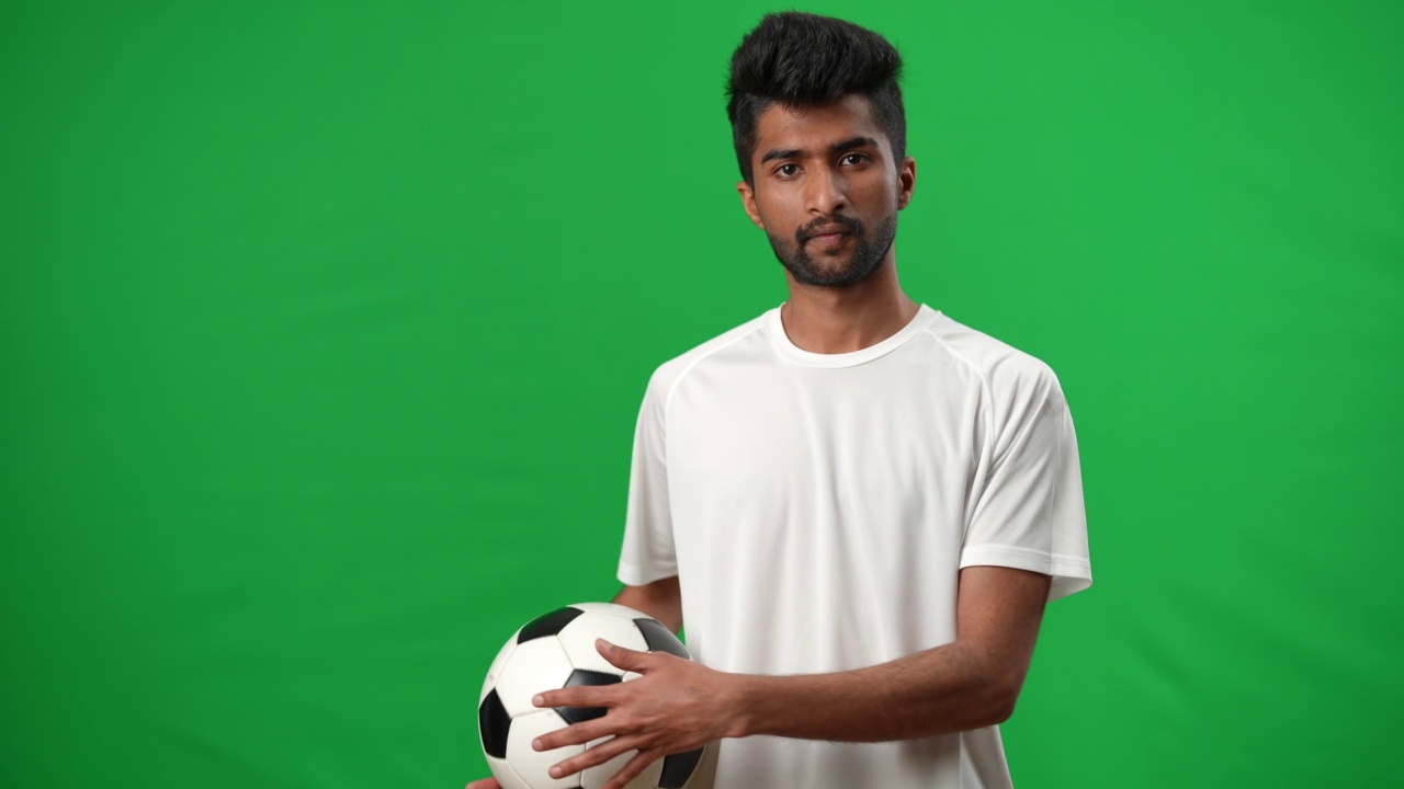 自信积极的中东足球运动员的肖像在绿色屏幕上与足球摆姿势。英俊的年轻运动员的中等镜头站在chromakey背景看相机。视频素材