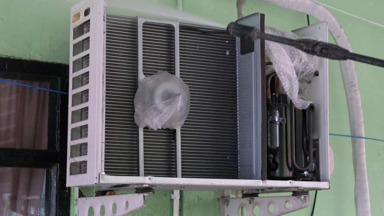 工作人员对空调压缩机进行喷水除尘。空调系统维护。家庭清洁卫生的概念。视频下载