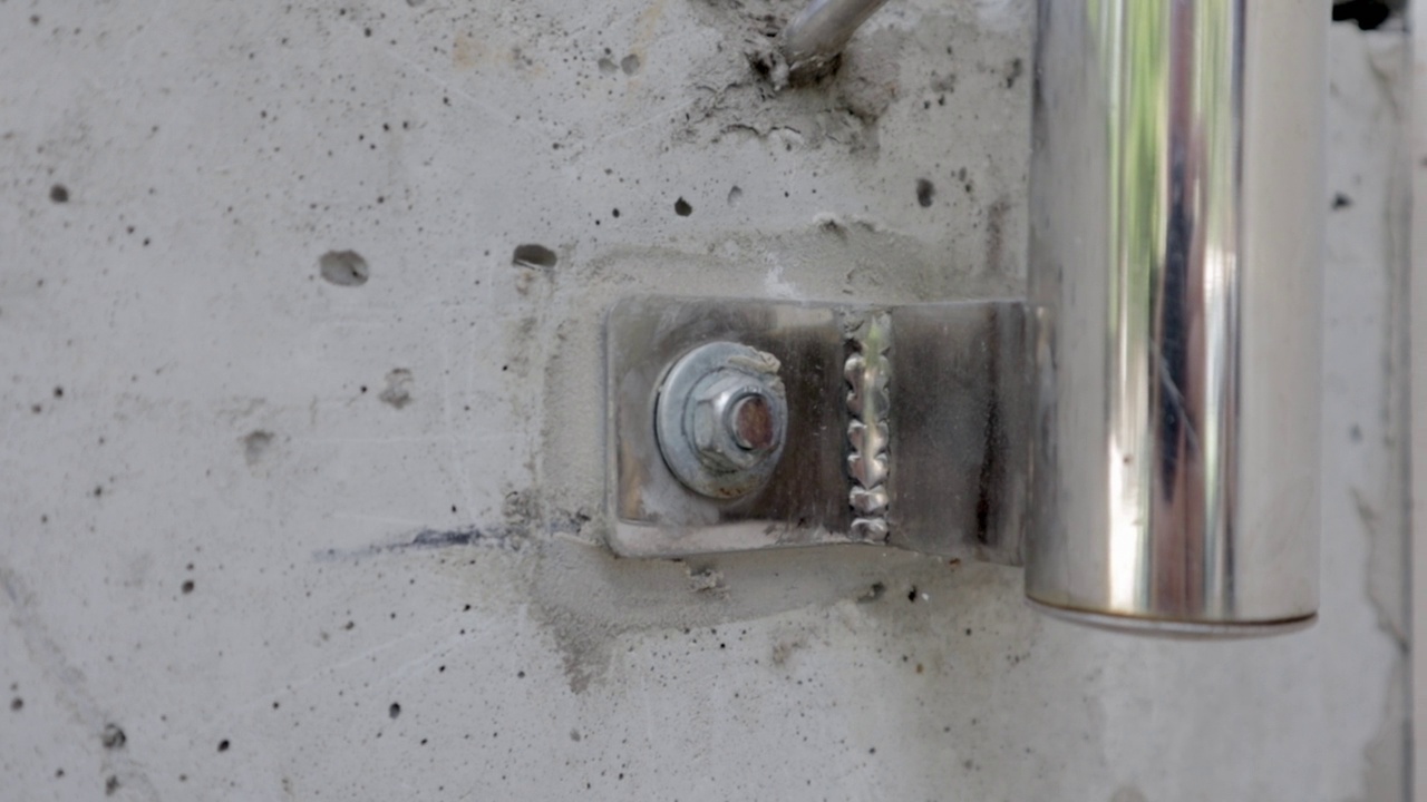螺栓在混凝土墙宏观特写库存镜头。将镀铬栏杆管用螺栓固定在混凝土墙上。螺栓与其他螺栓一起拧入混凝土中。灰色的金属视频下载