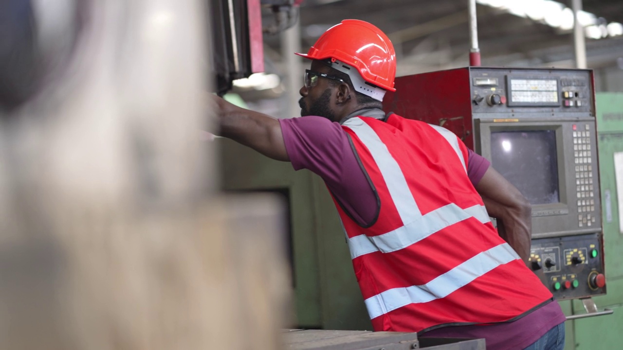 非裔美国男性工人在工业建筑中操作控制大型机器。维修和保养机器。安全工作性能。视频素材
