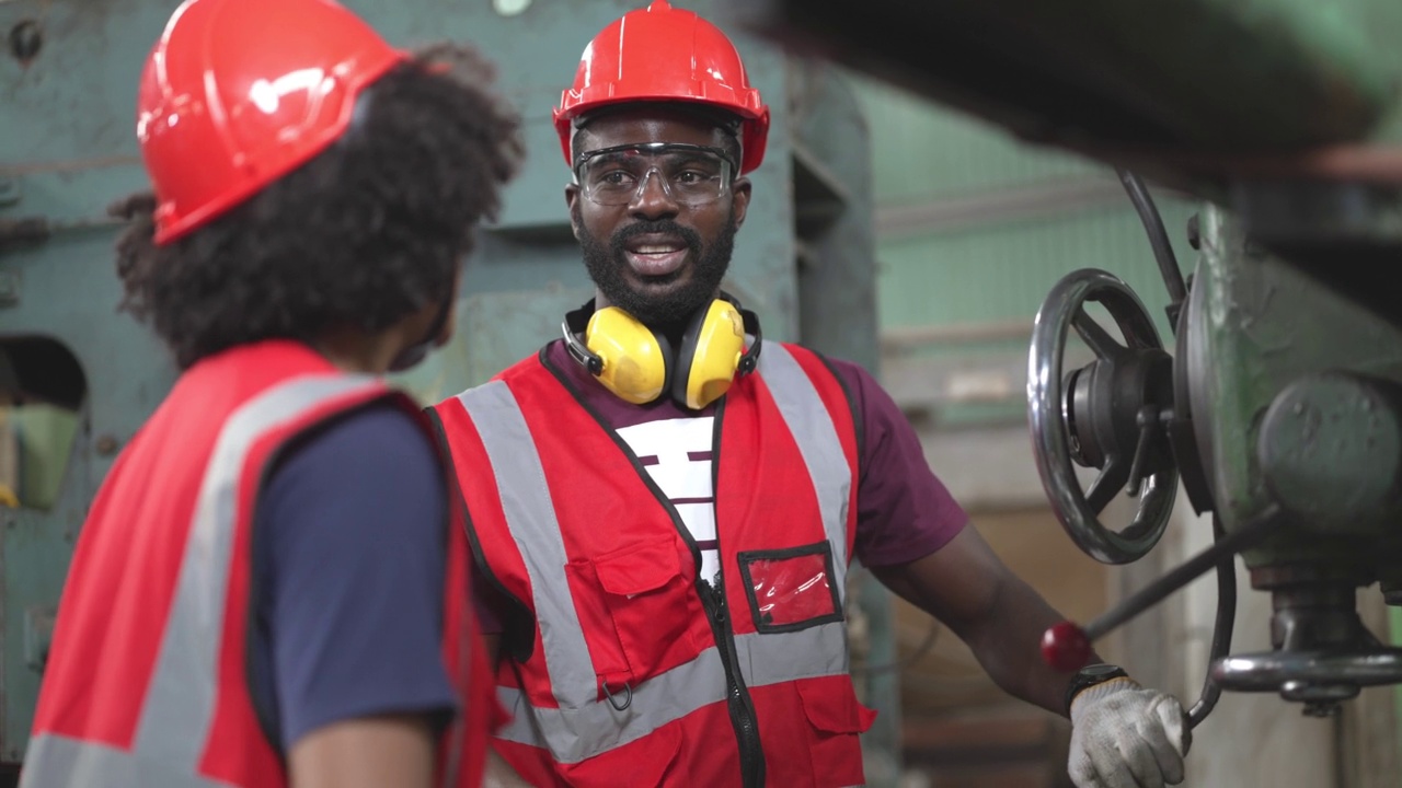 非裔美国男性工厂工人操作着大型机器，在工业建设中与同事一起工作和讨论。维修和保养机器。安全工作性能。视频素材