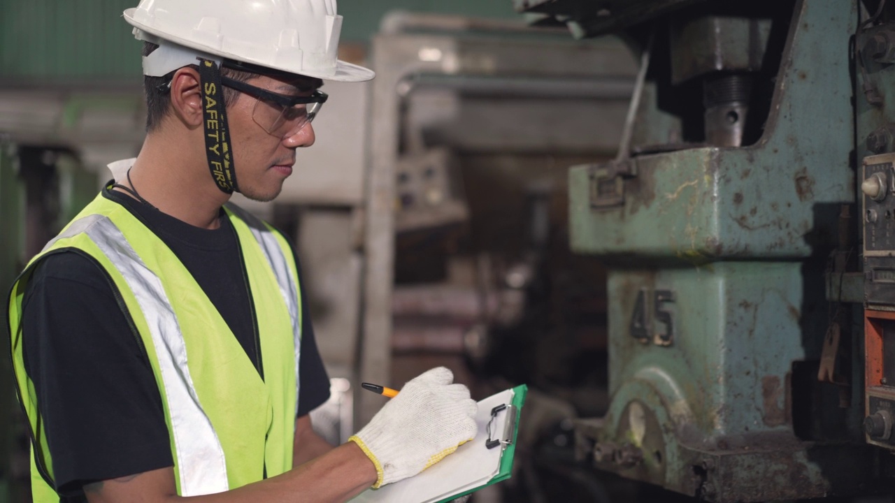 穿着安全服的亚洲男性工程师或工厂工人在工业建筑现场检查大型机器时，在检查记录板上写下检查记录。维修和保养机械的概念视频素材