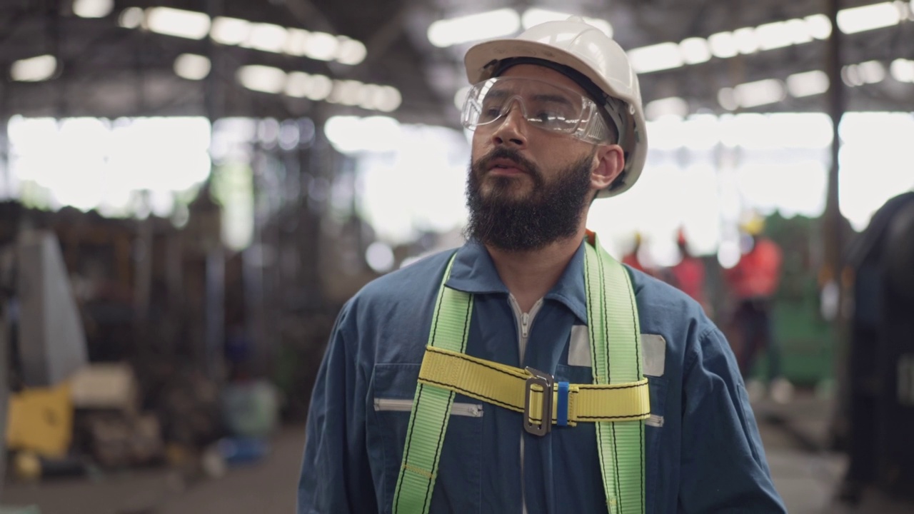 男工程师或技术工人穿着安全制服，戴安全帽和防护眼镜在工业工厂里行走。在建筑工地工作的自信机械师视频素材