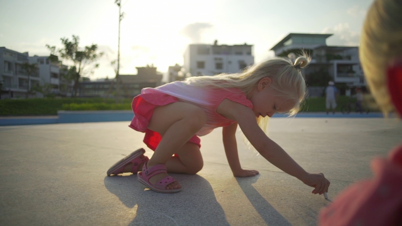 有趣的金发小女孩在操场上画粉笔在日落快速慢动作视频素材