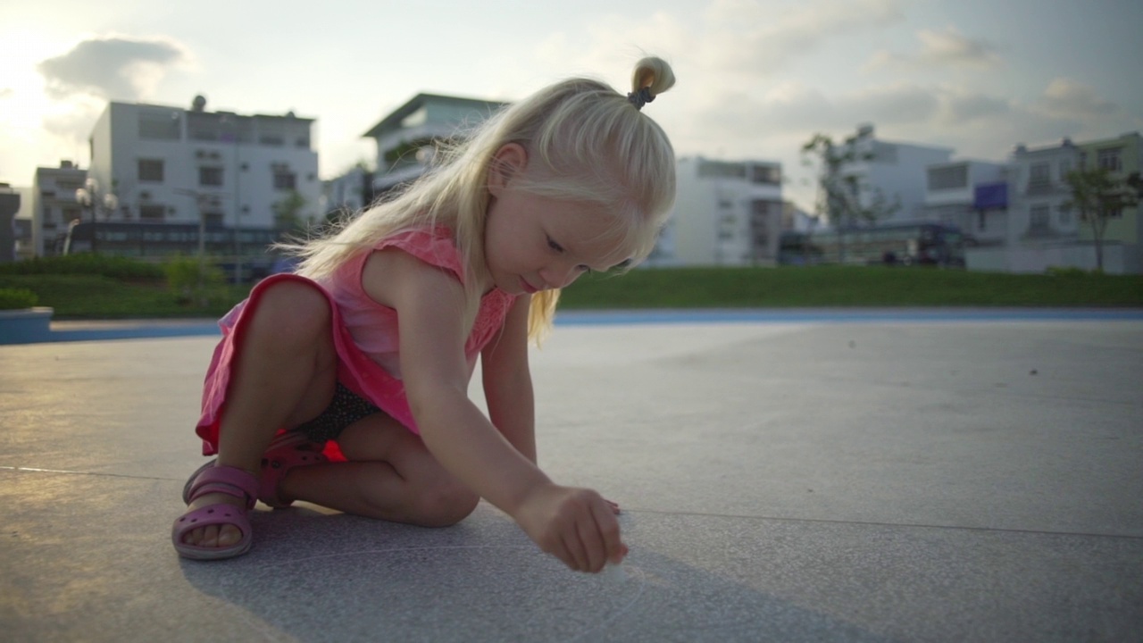 有趣的金发小女孩在操场上画粉笔在日出时快速慢动作视频素材