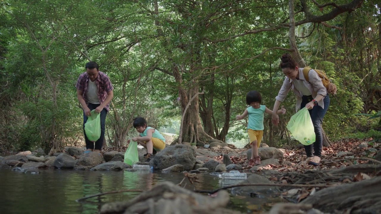 在河上，一个亚洲家庭志愿者捡起一个塑料瓶。视频素材