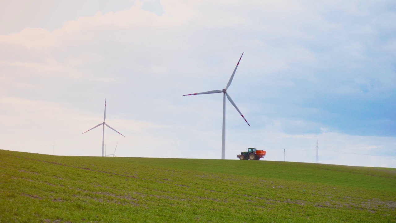 强大的农用拖拉机，农田喷洒化肥，靠近大型风力发电机，产生可再生的绿色生态能源视频素材