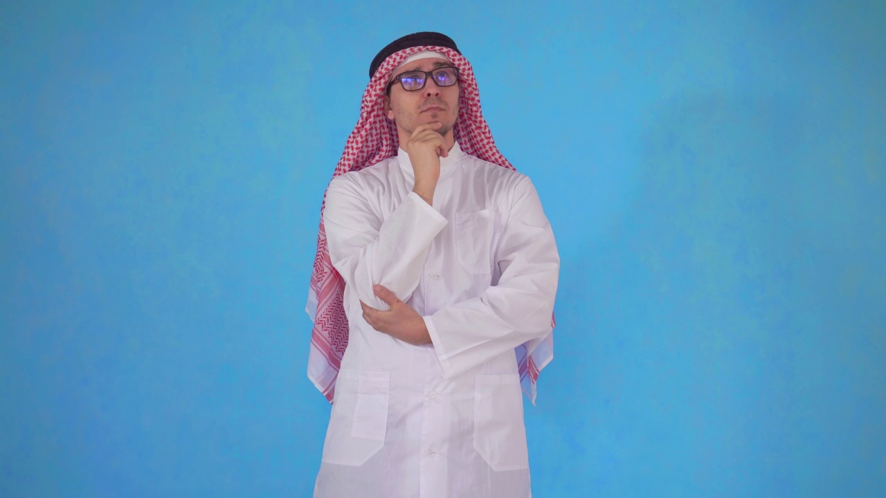 一个深思熟虑的阿拉伯人戴着眼镜站在蓝色的背景上视频下载