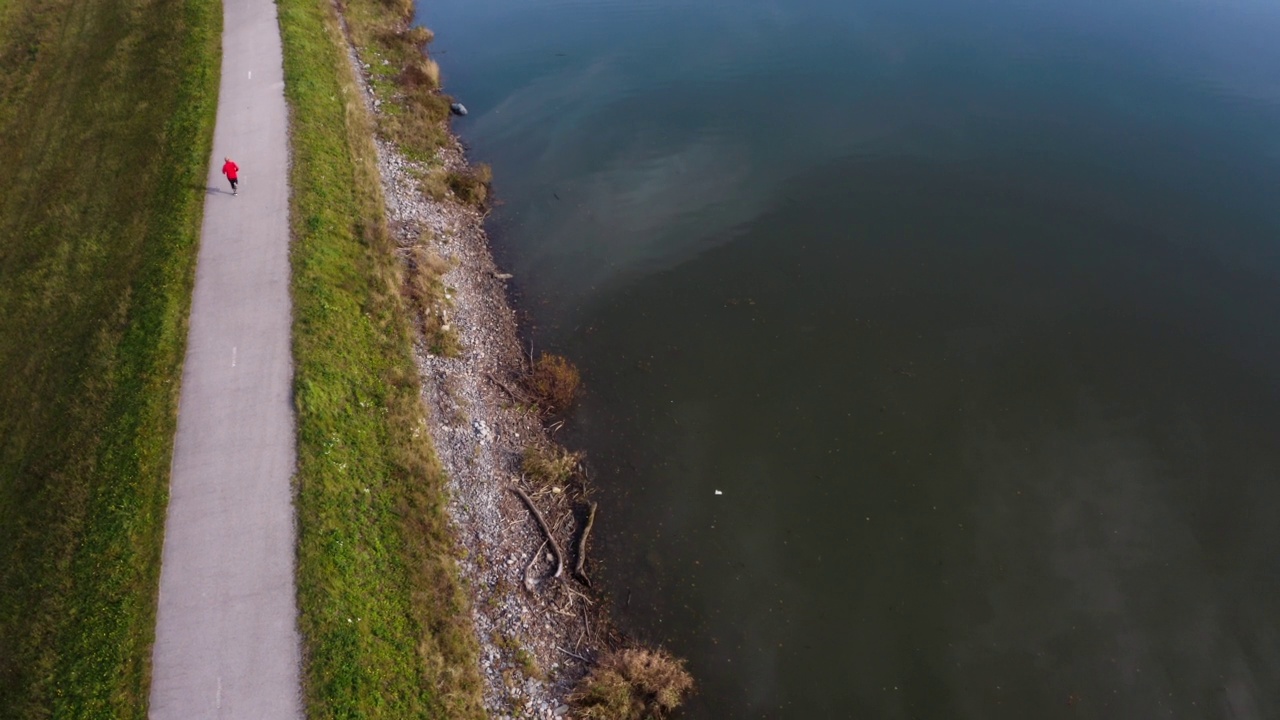 4K无人机拍摄的运动员穿着红色运动服在水库附近跑马拉松训练。体育的概念。视频素材