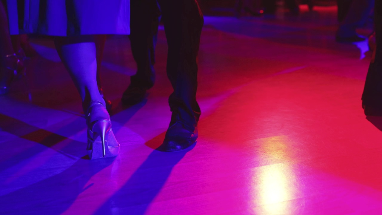 一对对舞伴的舞鞋，一对对舞伴在舞厅跳传统的拉丁阿根廷舞蹈milonga，跳探戈萨尔萨舞bachata kizomba，在木地板上的节日，紫色、红色和紫色的灯光视频下载