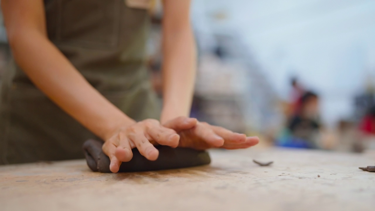 微笑的亚洲女艺术家陶艺家在围裙雕刻粘土陶瓷产品在工作间的工作台上。亚洲年轻女子站在附近手工制作粘土在工厂的壶制作艺术视频下载