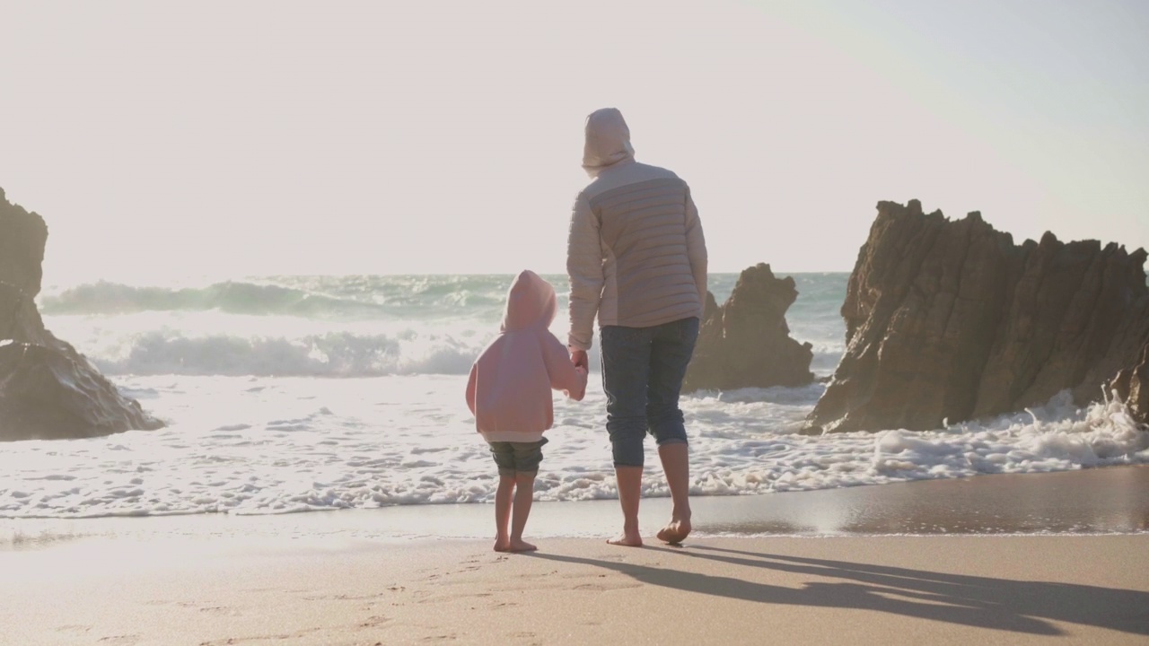 母亲和孩子在春天的海滩上玩海洋，穿着暖和的衣服，赤脚手持视频效果视频素材