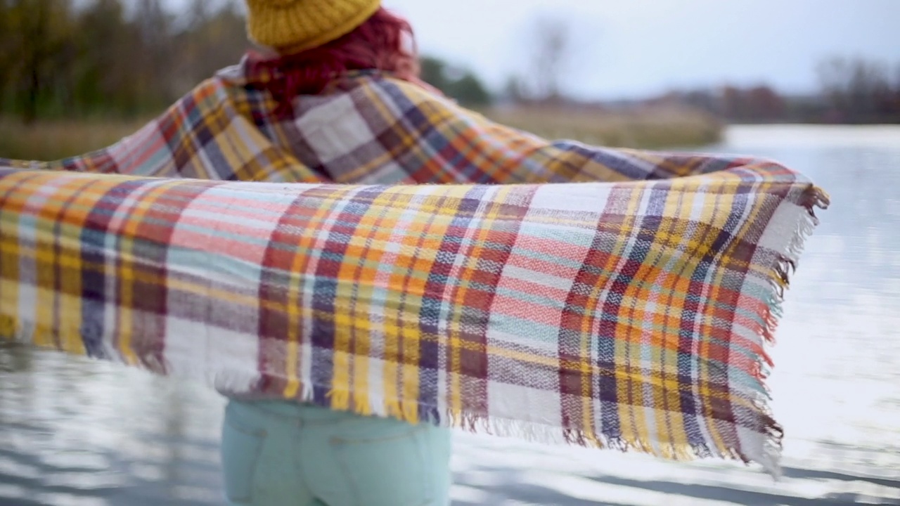 女人裹着温暖的毯子站在湖边的码头上视频下载