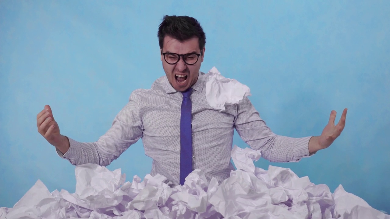 一个愤怒的办公室职员斜靠在蓝色背景上的一大堆皱巴巴的纸上视频素材