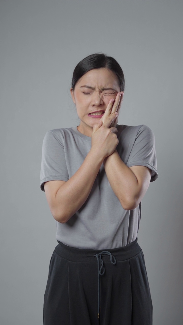 一名亚洲妇女患牙痛，孤立地站在灰色背景上。垂直视频4k分辨率。视频下载