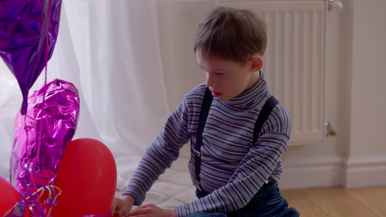 中等拍摄的肖像聚焦古玩自闭症男孩玩气球和看着相机。前视图高加索精神病顽皮儿童享受休闲在家室内。视频素材