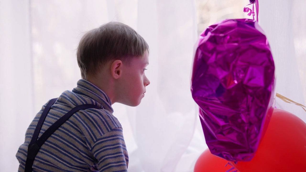 侧视图聚焦自闭症男孩注视着紫色的气球，表情集中。患有精神障碍的高加索儿童在家里检查新玩具。视频素材
