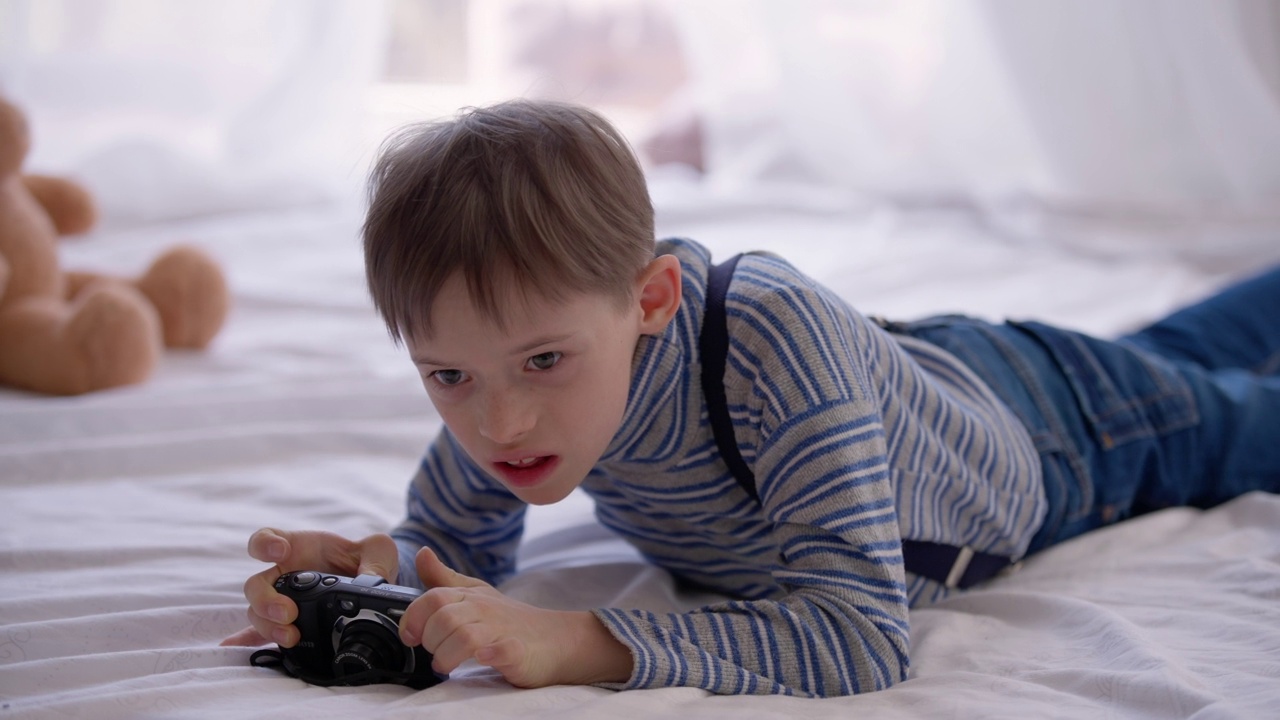 自闭症男孩躺在床上，表情凝重地检查摄像头。患有精神疾病的轻松的白人儿童在家里的卧室里玩耍的肖像。好奇和自闭症的概念。视频素材