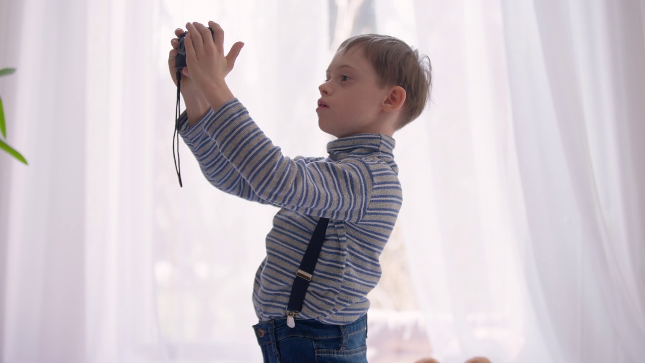 侧视多动症自闭症男孩在室内用相机拍照。有精神障碍的天才白人孩子喜欢站在家里。自闭症和活动的概念。视频素材