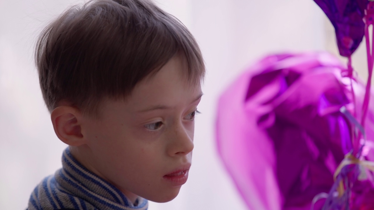 侧视图聚焦自闭症男孩欣赏室内的紫色气球。有精神障碍的高加索儿童在家里检查紫色玩具的特写肖像。视频素材