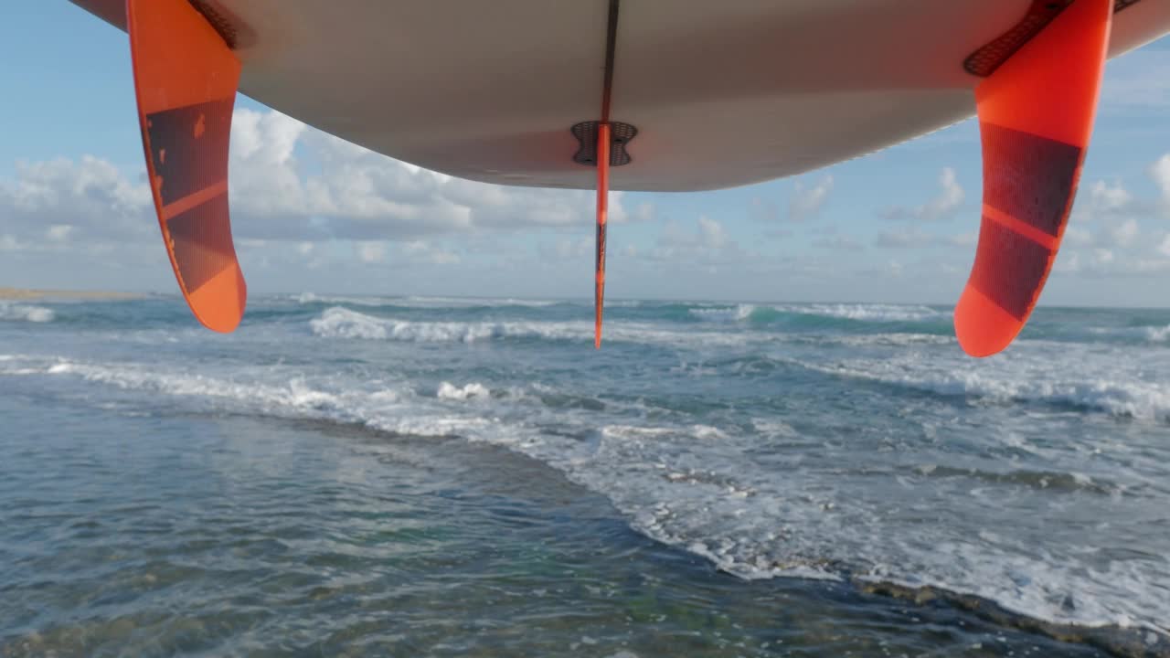 观点的看法。带有橙色鳍的冲浪板在海滩上对抗海浪。视频下载