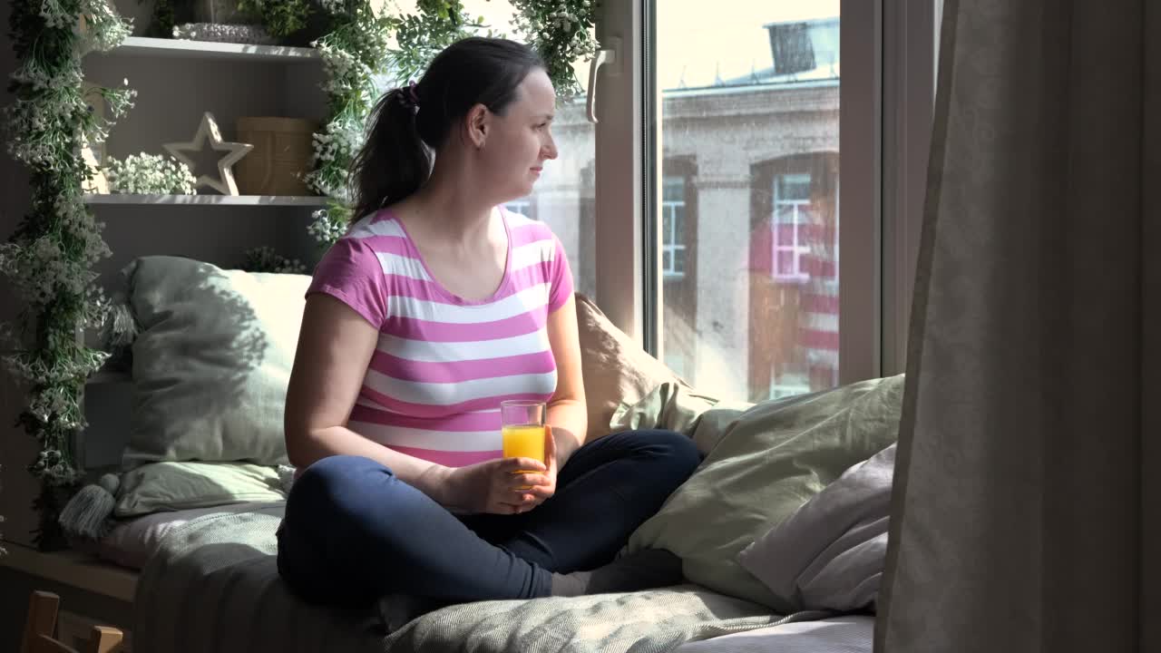 在窗台上喝新鲜果汁的孕妇视频素材