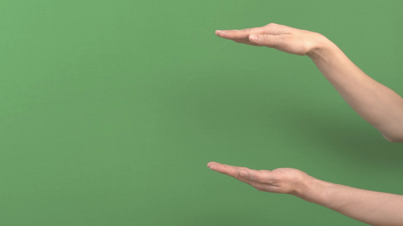 女人牵着手在手掌之间展示一些虚拟的、看不见的东西。女性手在绿屏色度键背景上为广告扩展拷贝空间视频下载