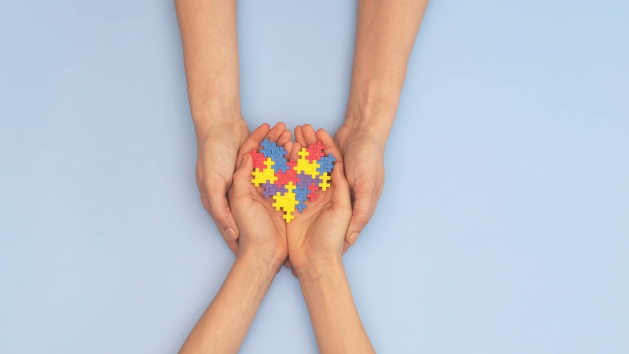 世界自闭症意识日的概念。女人和孩子手握拼图心在浅蓝色的背景。俯视图视频下载