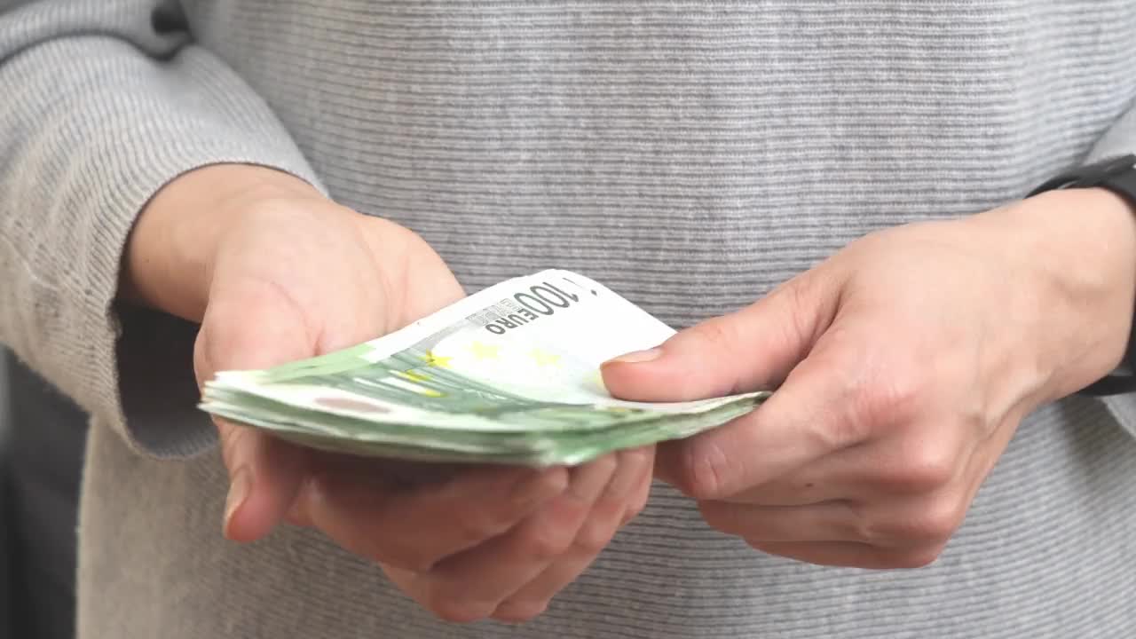 忧心忡忡的女人手里拿着现金欧元钞票。现金支付概念，家庭预算，财务决策，大采购，投资。一名妇女手中拿着一叠100欧元钞票。4 k的视频视频素材