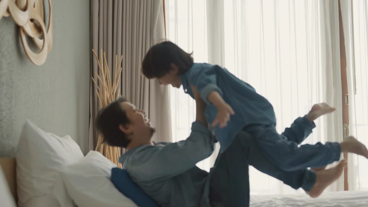 父亲抱着孩子，儿子在床上玩飞机。视频下载