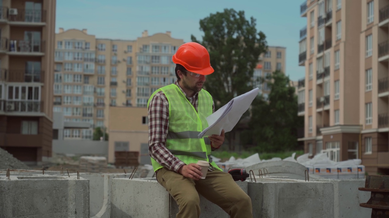 男性专业工头建筑商年轻的白人男子在施工现场工作与图纸的技术文件，戴安全帽，眼镜，反光背心。主题建设和工作中的人。视频素材