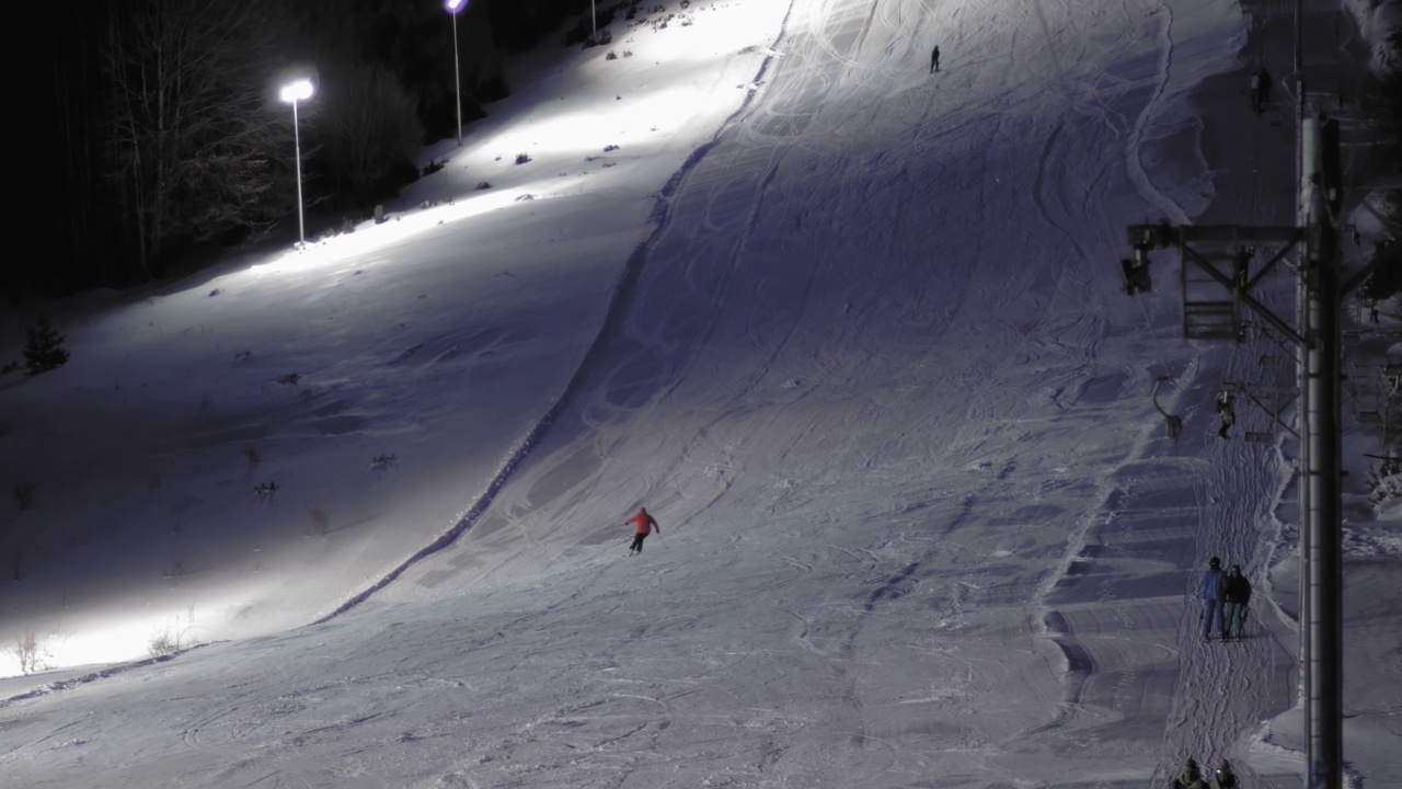 滑雪者在有灯光的滑雪道上使用滑雪缆车到达坡顶进行夜间滑雪视频素材