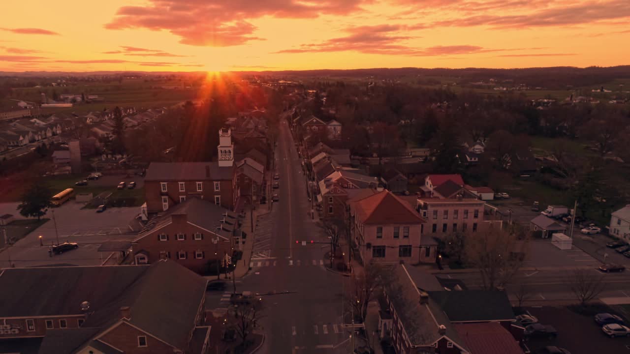 在一个春天的日出，当太阳打破地平线时，沿着主要街道旅行的一个小镇的高空鸟瞰图视频下载