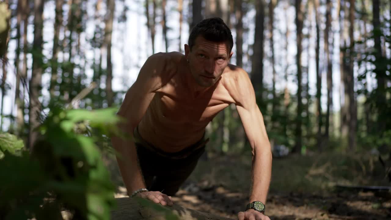 正面视图自信的肌肉男做俯卧撑夏天春天森林户外。集中的高加索健美运动员在阳光下锻炼躯干。运动和生活方式的概念。视频下载