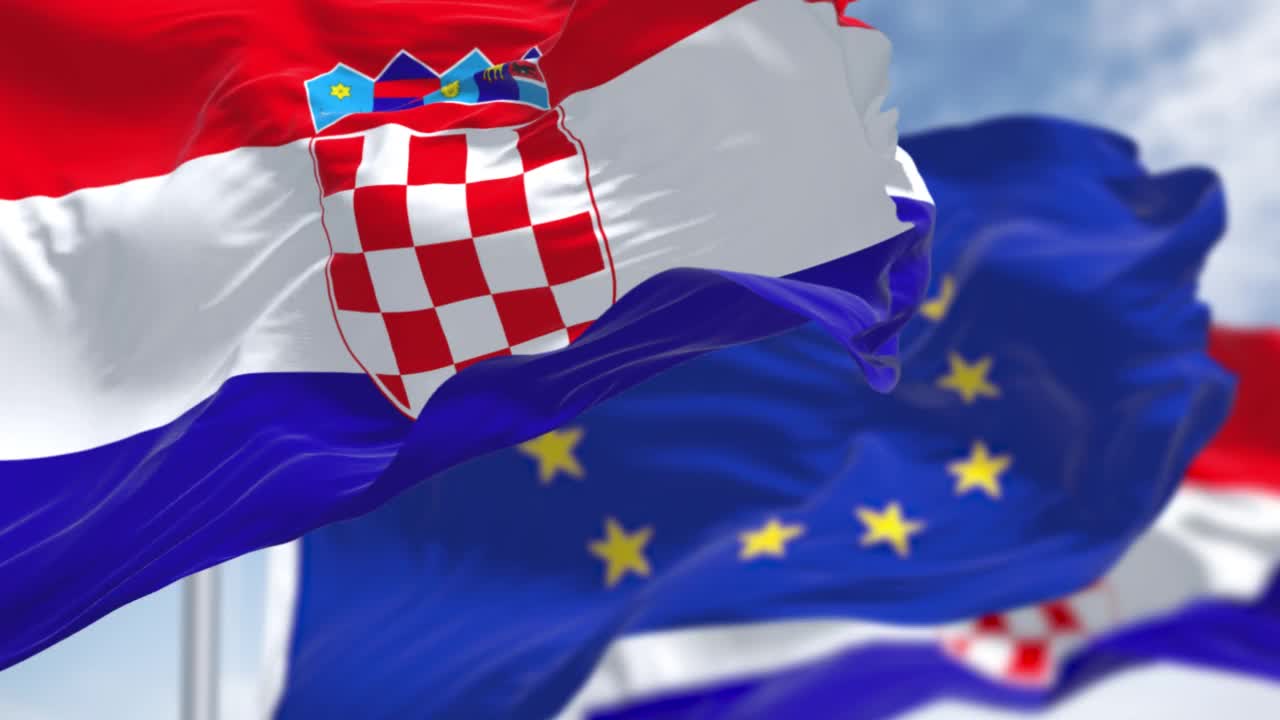 在晴朗的日子里，克罗地亚国旗在风中飘扬，背景是模糊的欧盟旗帜。视频素材