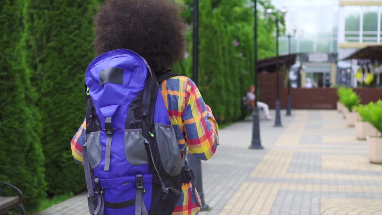 黑人女游客与一个爆炸头发型和背包背后后景慢莫城市景观视频下载