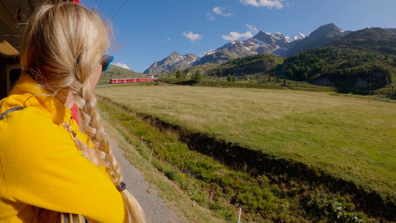 兴奋快乐的女人，微笑着探出车窗。旅行的女人在瑞士红色火车旅行低谷阿尔卑斯山视频下载