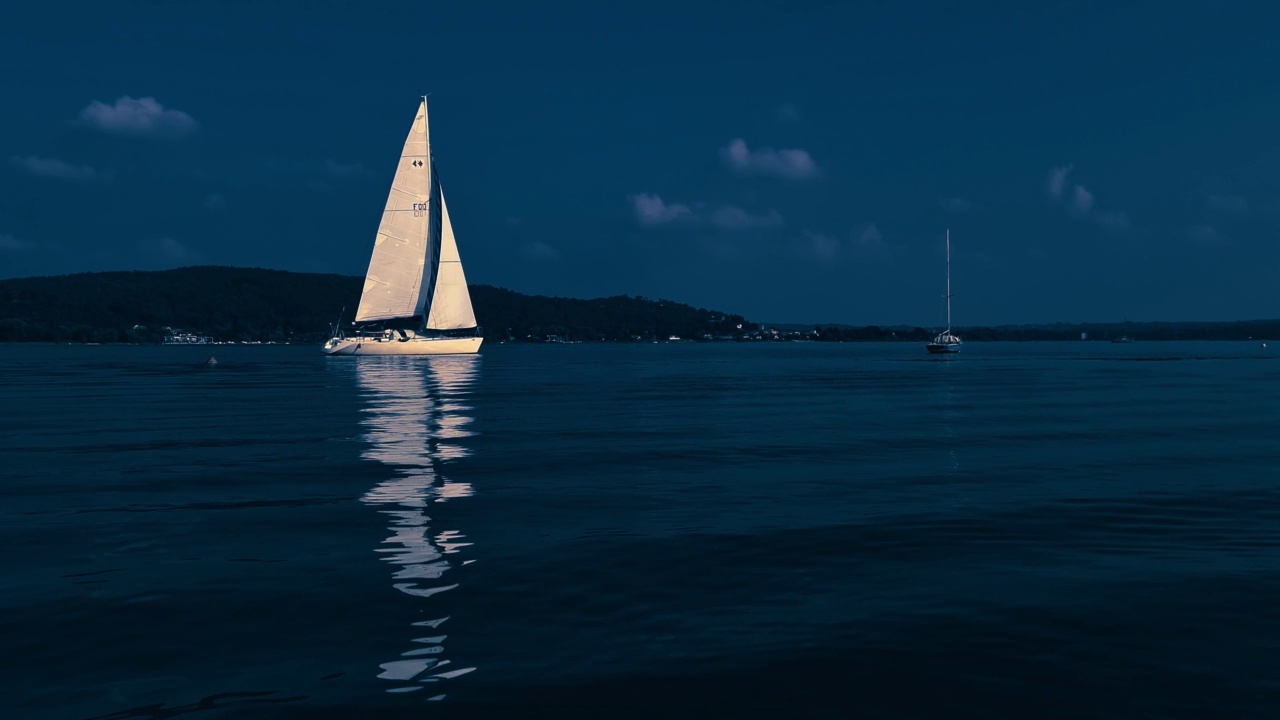 小船在平静开阔的湖水中航行的夜间彩色镜头。慢动作的低角度视频素材