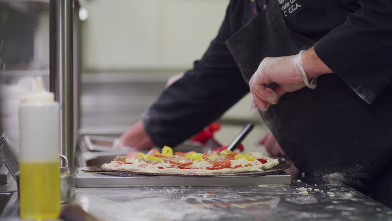 餐厅厨房里，厨师在披萨里加辣椒片和橄榄。视频下载