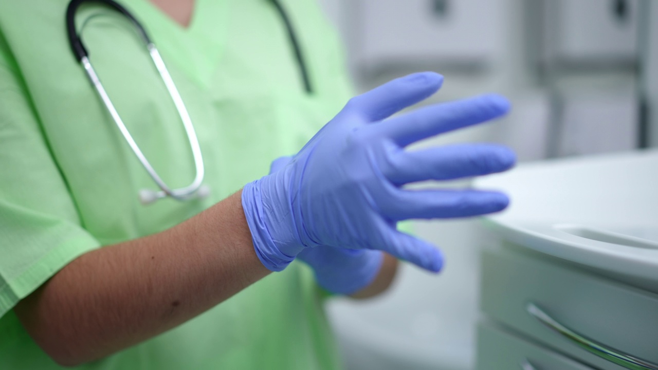 在室内的慢镜头中，不知名的医生正戴着医疗手套。年轻的白人妇女准备在医院做手术。保健和卫生观念。视频素材