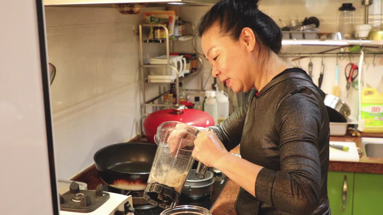 亚洲中年妇女用搅拌机准备健康食品视频下载