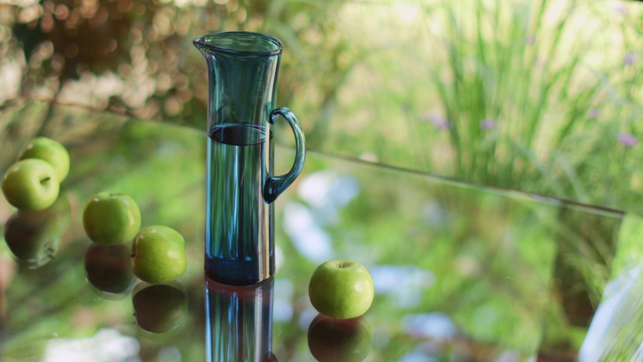 高高的水罐和绿苹果放在玻璃桌上视频下载