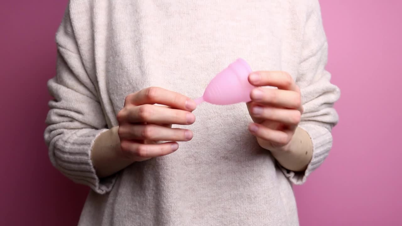 一个穿着毛衣的难以辨认的女人展示了一个粉红色的月经杯。视频素材