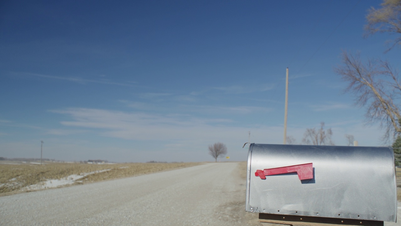画面描绘了一个乡村邮箱在一个荒凉的砾石路的边缘与蓝色的天空。视频下载