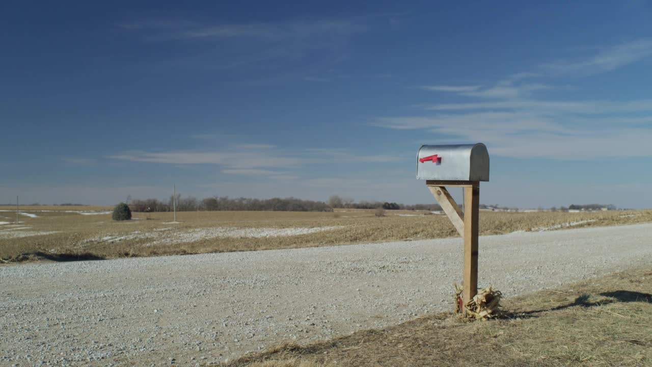 画面描绘了一个乡村邮箱在一个荒凉的砾石路的边缘与蓝色的天空。视频下载